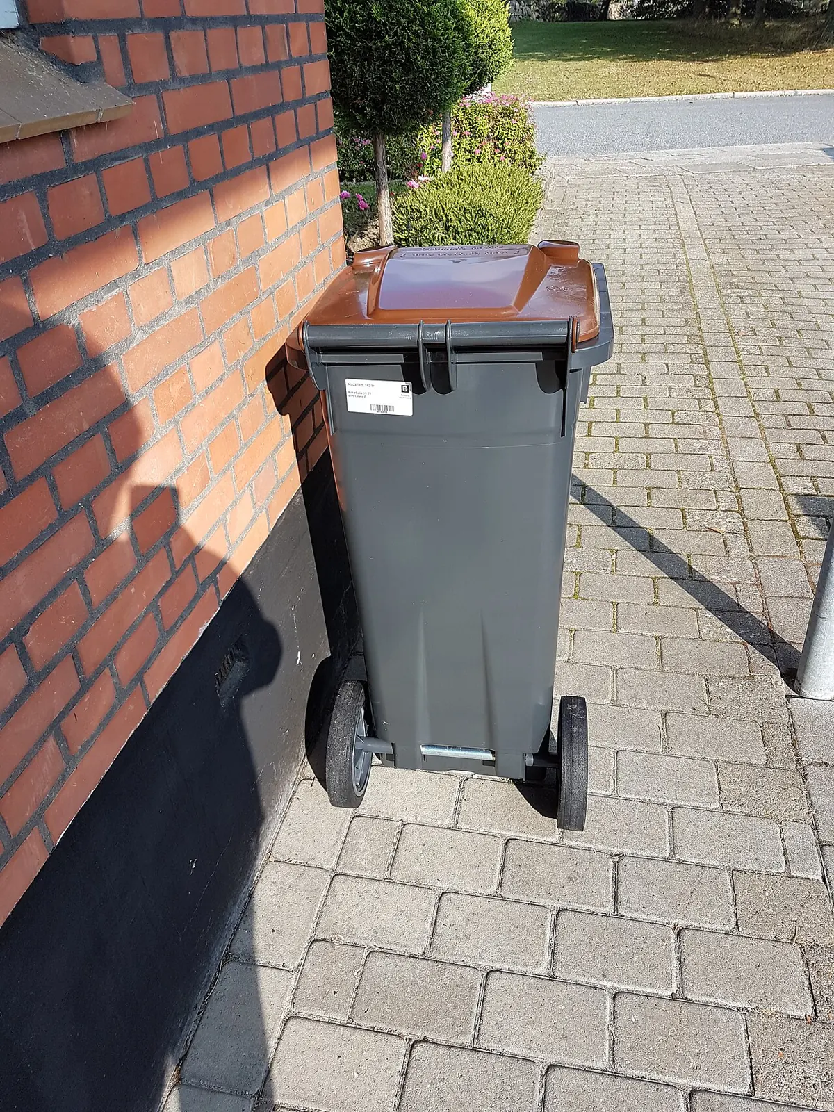 Wheeled trash bin standing on a brick sidewalk